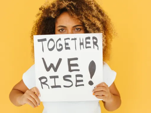 Female holding a sing in front of her face that reads "Together We Rise"