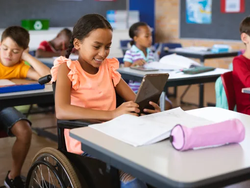 Disabled African American girl using a tablet while sitting in wheelchair at elementary school