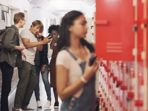 Teenage girl standing at her locker and being bullied at high school