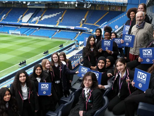 Students in a football stadium holding signs that read "No to Hate"