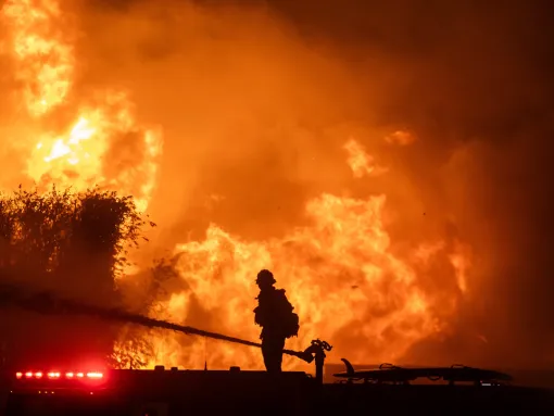 A firefighter stands on top of a fire truck to battle the Palisades Fire while it burns homes on the Pacific Coast Highway amid a powerful windstorm on January 8, 2025 in Los Angeles, California. (Apu Gomes/Getty Images)