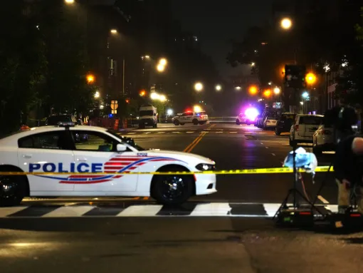 A police car and crime scene tape block off a street at night.