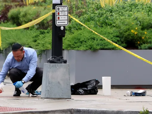 An embassy official cleans blood off the sidewalk at the shooting location outside of the Capital Jewish Museum on May 22, 2025, in Washington, DC