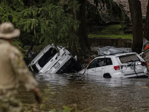 Vehicles sit submerged as a search and rescue worker looks through debris for any survivors or remains of people swept up in the flash flooding on July 6, 2025, in Hunt, Texas